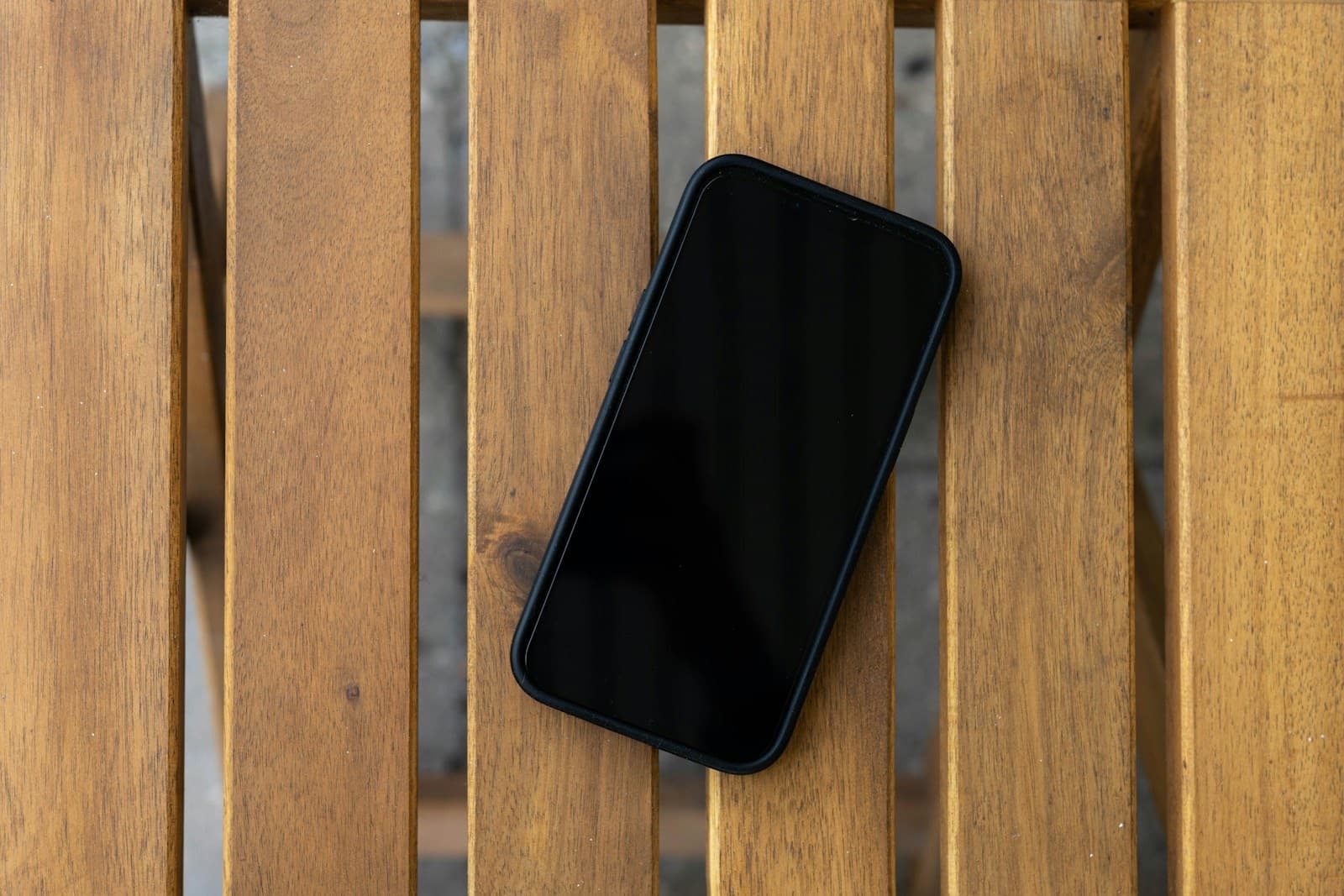 A phone, screen off, resting on warm wooden slats