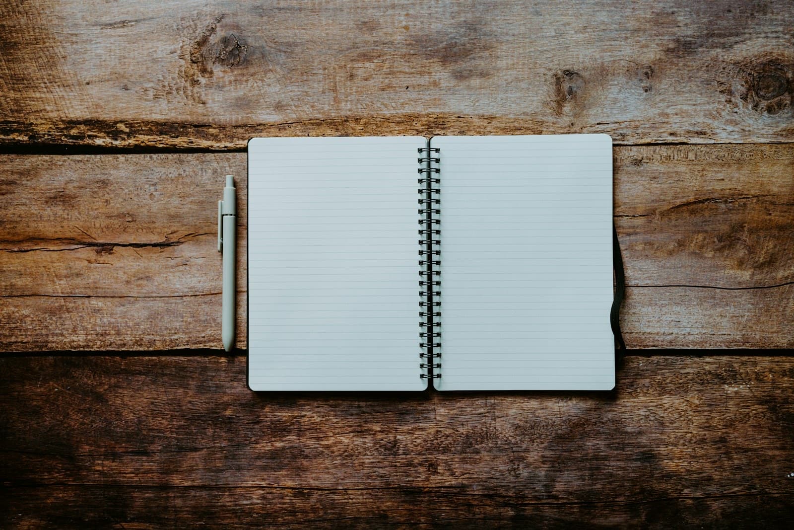 Open spiral notebook with blank pages and a pen set down on a wooden table