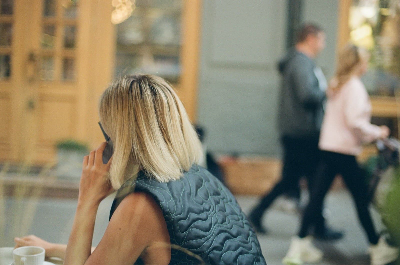 Woman seen from behind talking on the phone at an outdoor café table with a coffee