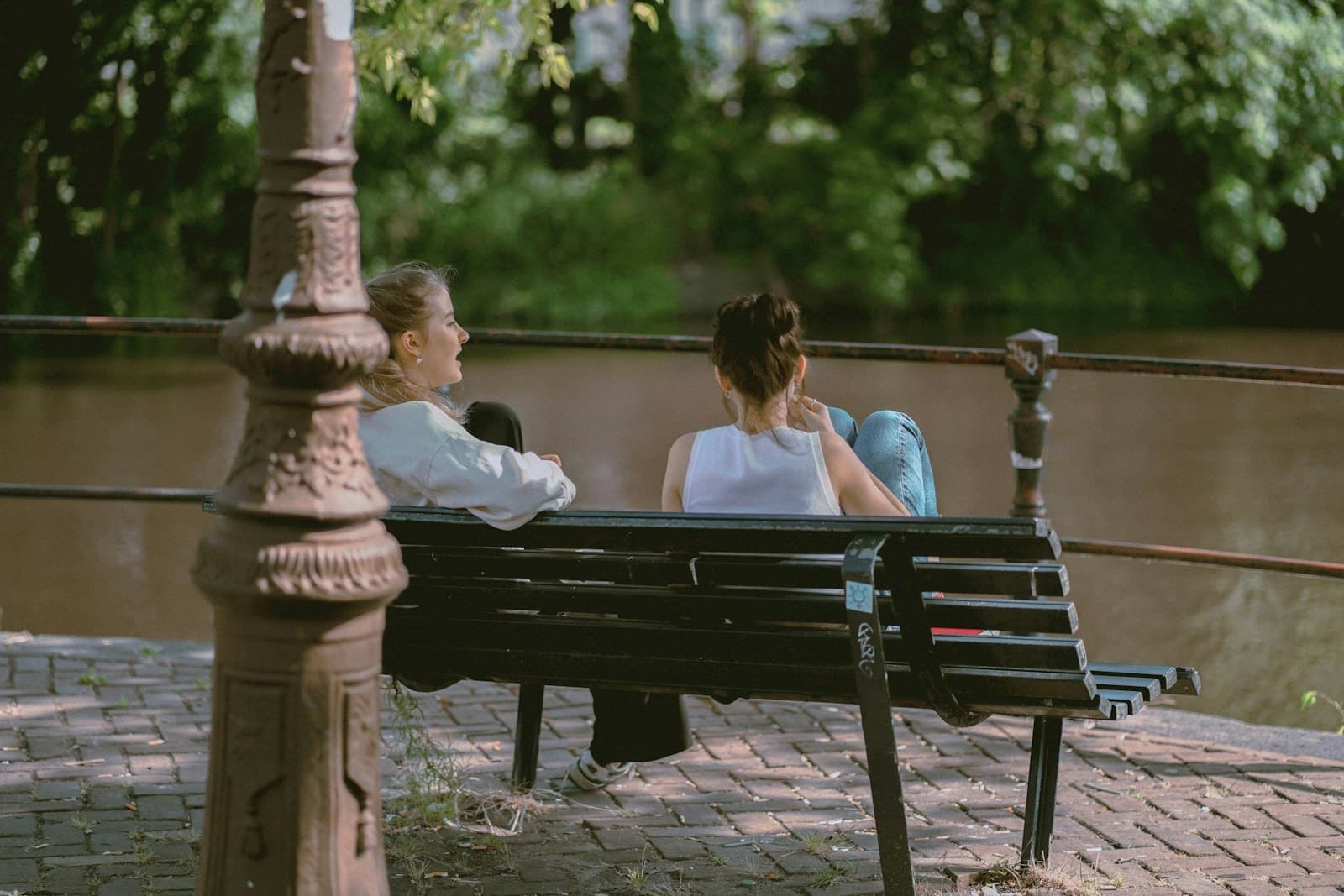 Two women talking on a riverside bench, seen from behind