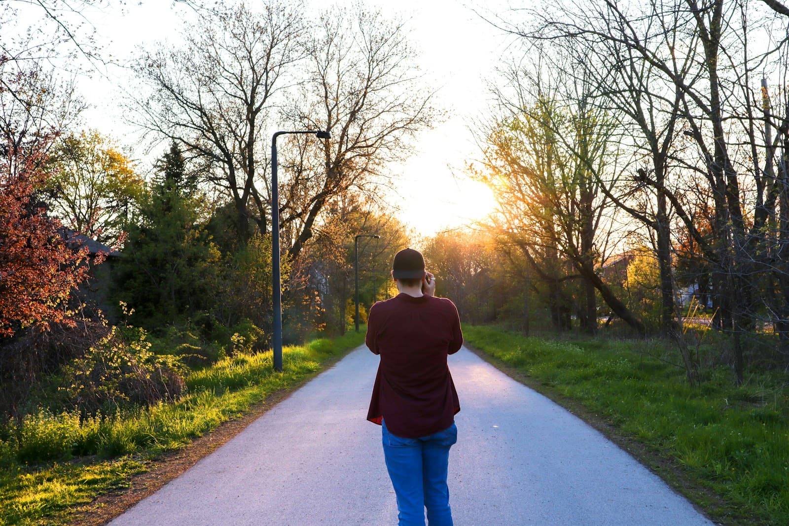 Man walking a tree-lined path at sunset with a phone to his ear