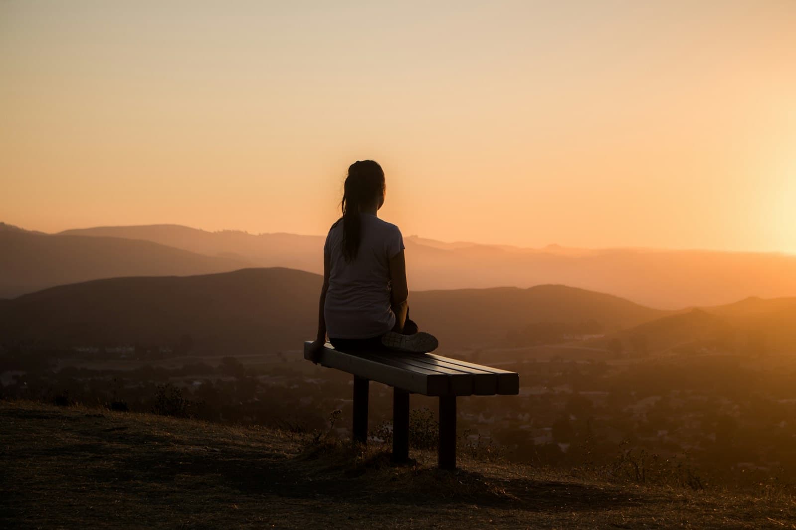 Woman on a bench at golden hour overlooking hills