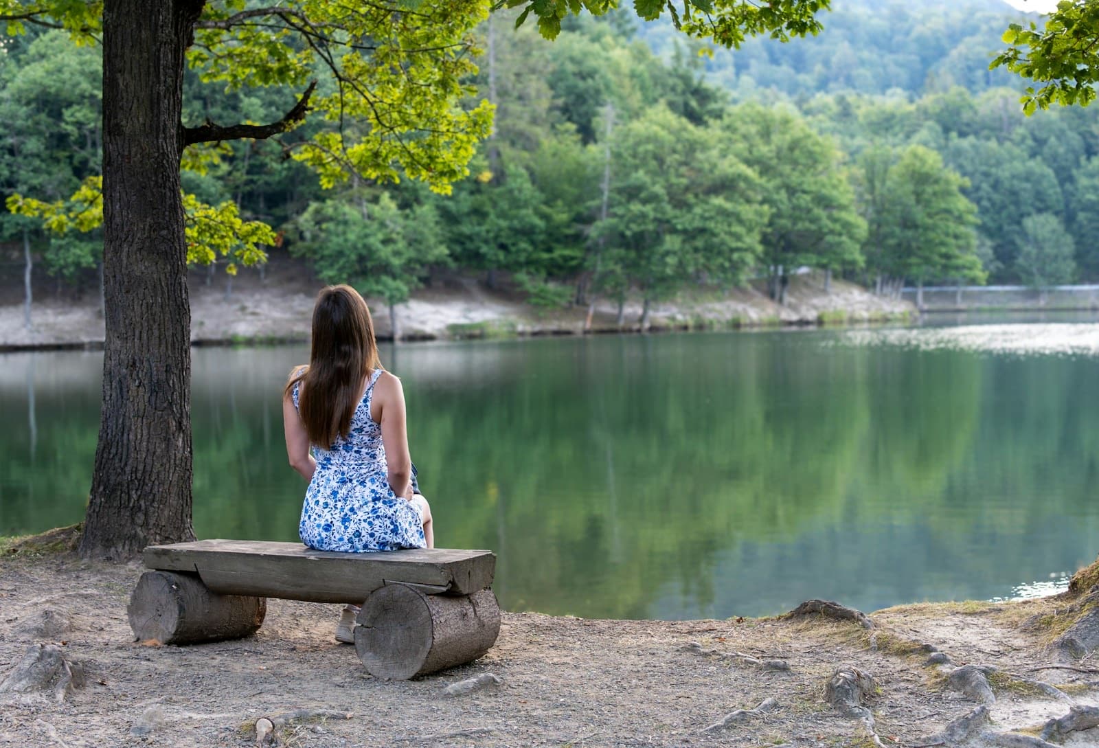 Woman sitting on a log bench at the edge of a calm lake